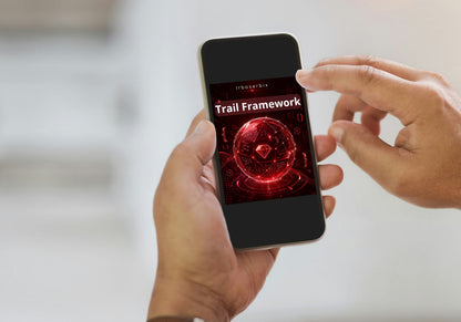 A person holding a smartphone with a black bezel displaying a red and black digital interface titled 'Trail Framework'. The person's hands are visible holding the phone, with a softly blurred light gray background.